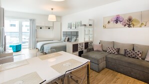 A modern hotel room with a bed, a sofa, a dining table, and a large window. - Super-Apartamenty Love Deluxe (Poznan)