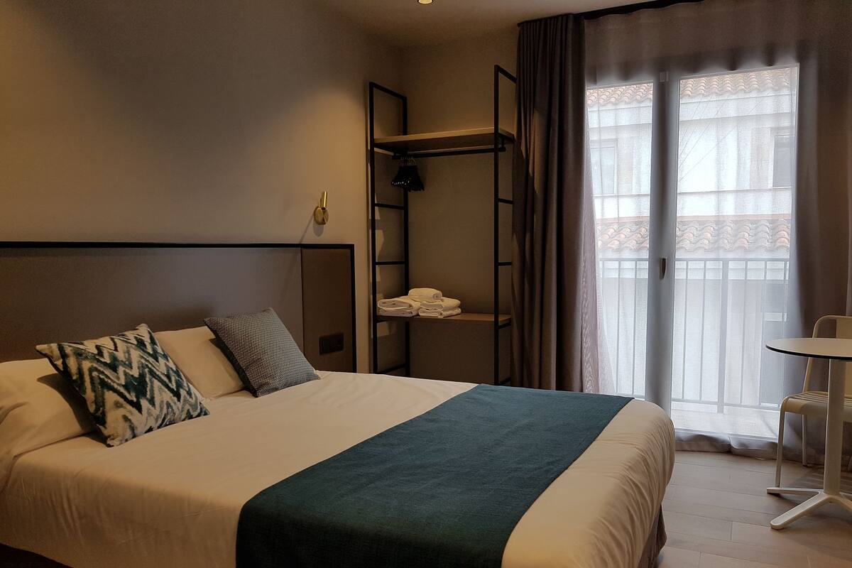 A hotel room with a bed, a bunk bed, a small table, and a window with curtains.