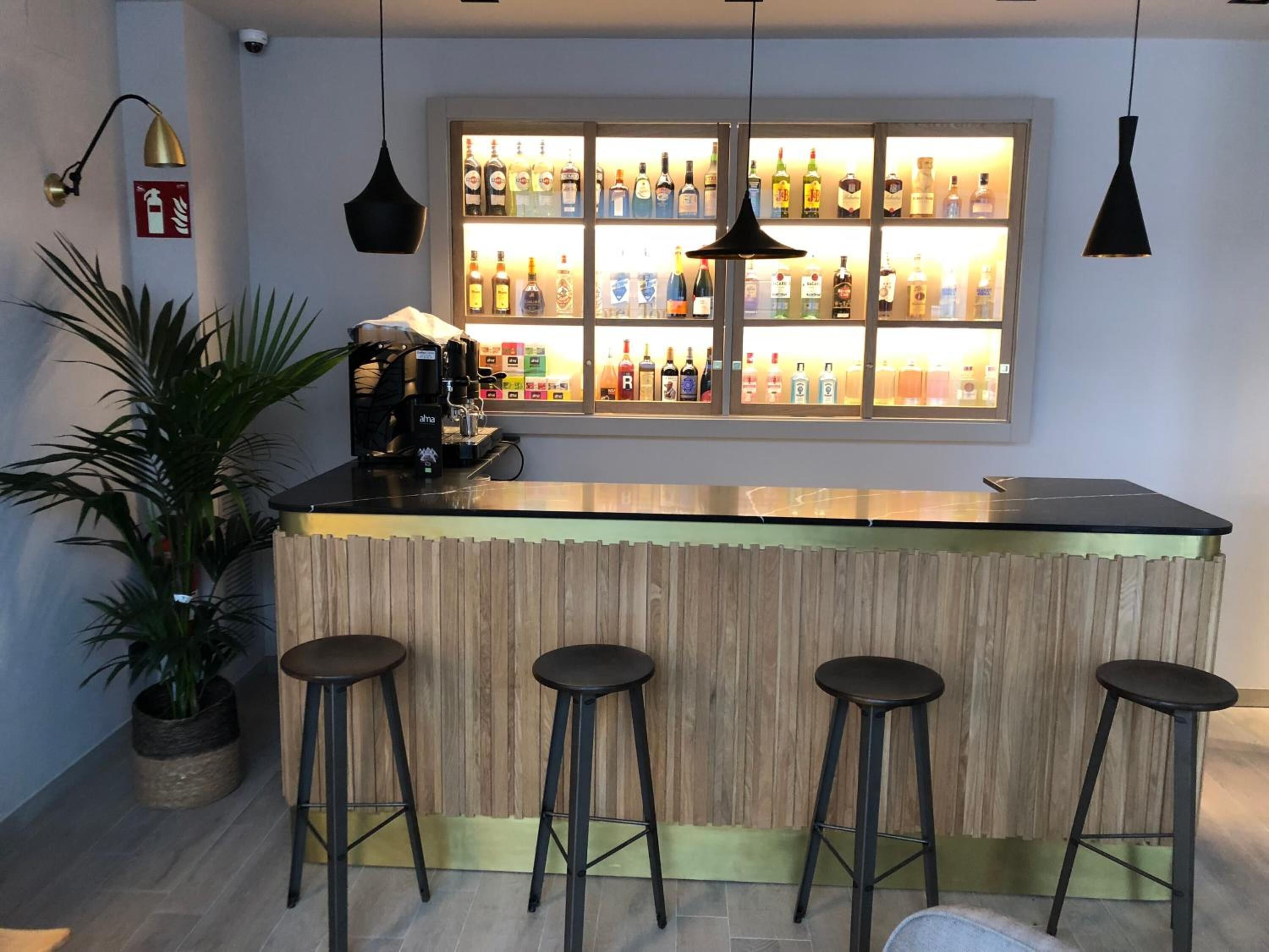 A bar area with a wooden counter, four stools, a coffee machine, and a shelf of liquor bottles.