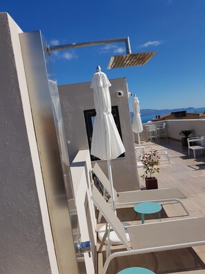 A rooftop terrace with white umbrellas, outdoor seating, and a view of the sea. - Hotel Torrent (L'Escala)