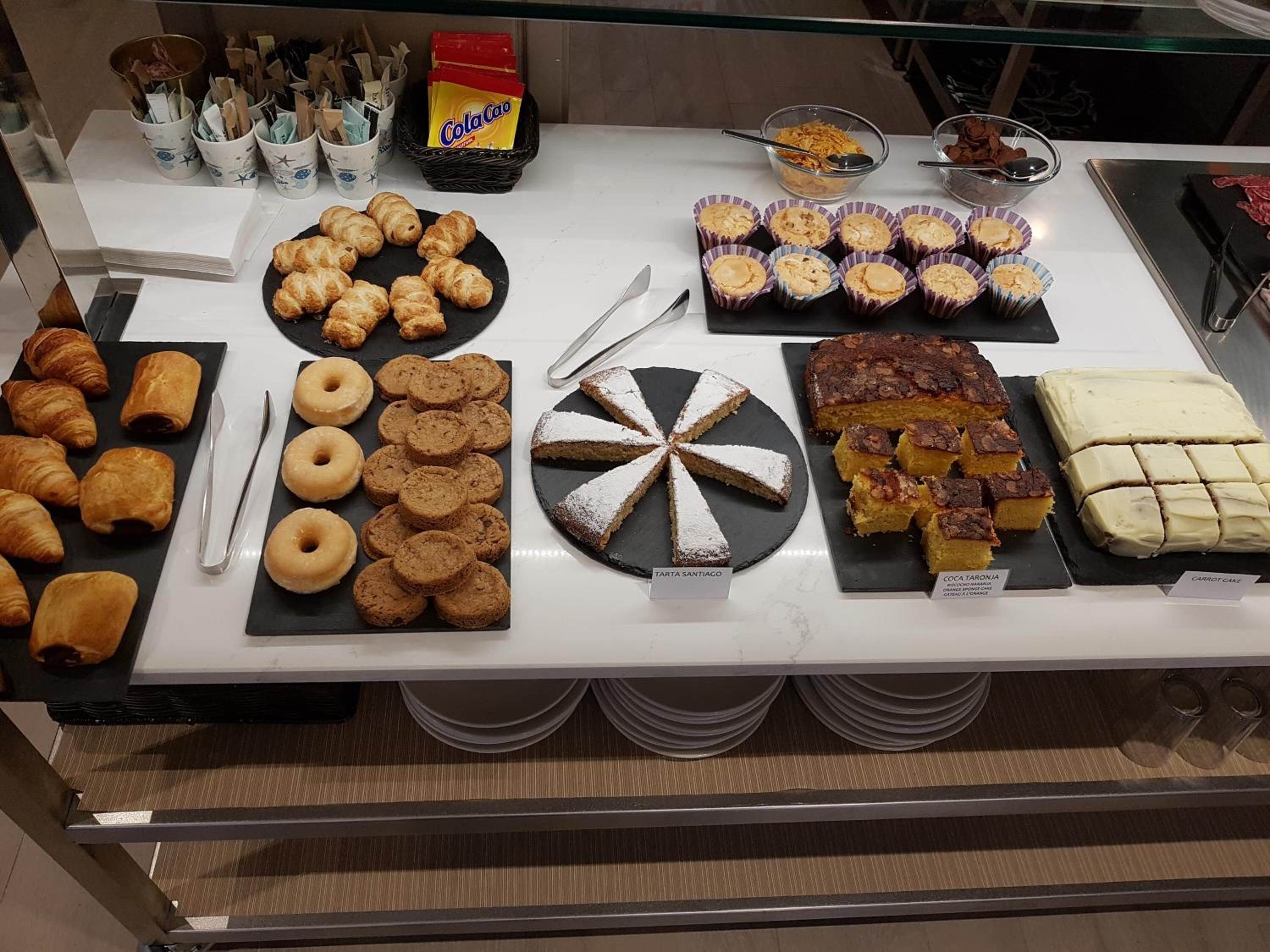 Un bufé con diversos pasteles y postres, incluyendo croissants, rosquillas y pasteles.