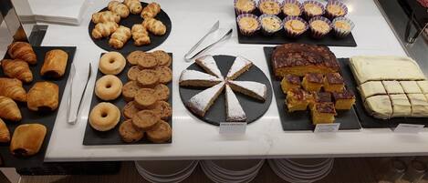 Un bufé con diversos pasteles y postres, incluyendo croissants, rosquillas y pasteles.