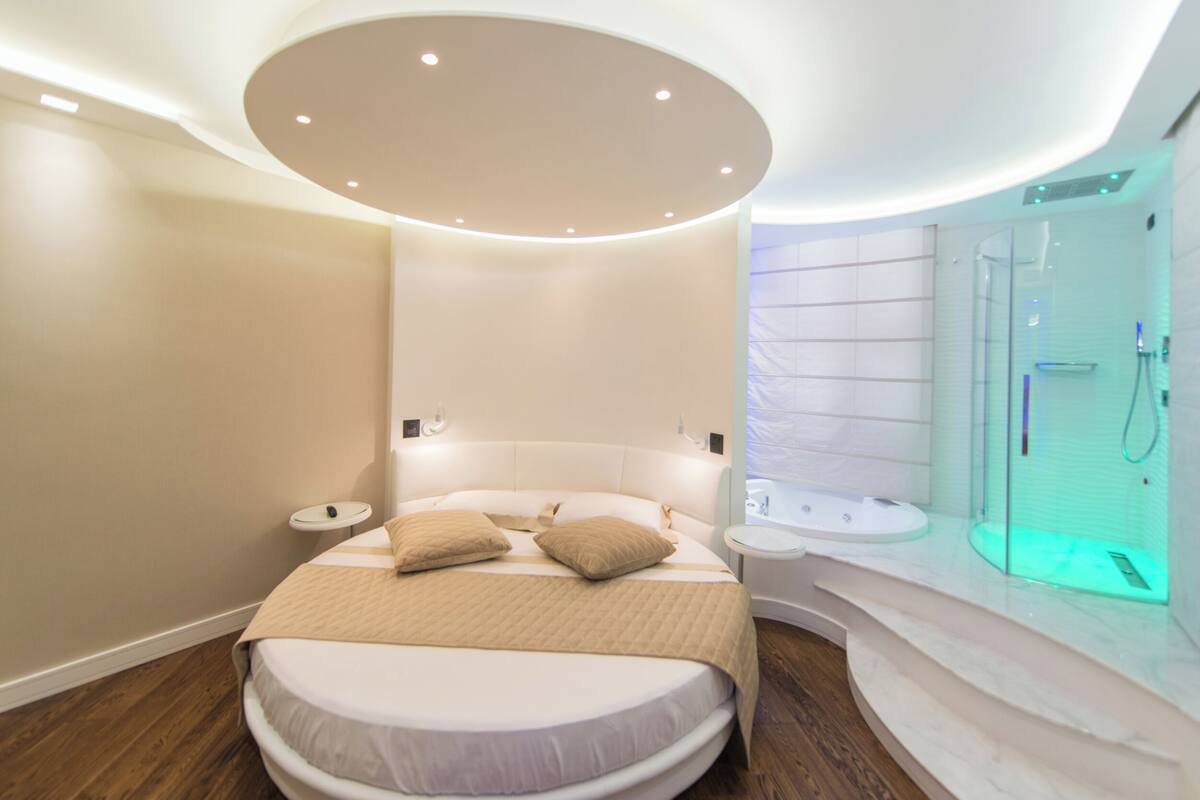 A modern bedroom with a curved bed, a built-in sink, and a glass-enclosed shower.