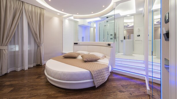 A modern bedroom with a circular bed, a glass shower enclosure, and a well-lit ceiling. - LUX suites in Roma (Rome)