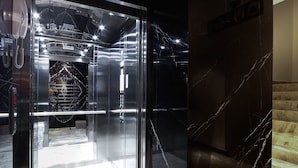 Un ascensor moderno con puerta de vidrio, paredes de mármol y espacio interior visible.