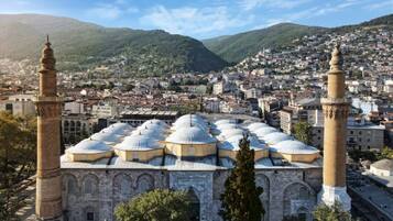 A historic building with multiple domes and minarets, surrounded by a densely populated urban area with mountains in the background.