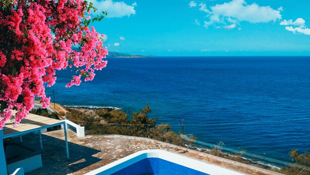 A pool with a clear view of the sea, surrounded by a stone patio and pink flowers. - Karma Minoan (Agios Nikolaos)
