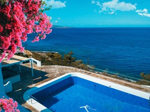 A pool with a clear view of the sea, surrounded by a stone patio and pink flowers. - Karma Minoan (Agios Nikolaos)