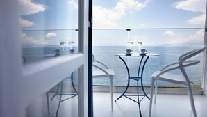A balcony with a table and two chairs, overlooking a body of water with mountains in the distance. - Karma Minoan (Agios Nikolaos)