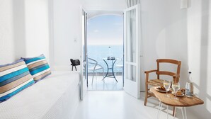 A hotel room with a balcony, a dining table with chairs, a bottle of water, and a view of the sea. - Karma Minoan (Agios Nikolaos)