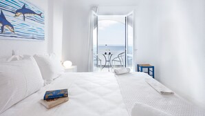 A hotel room with a bed, a small table, a chair, a painting of dolphins, and a view of the sea. - Karma Minoan (Agios Nikolaos)