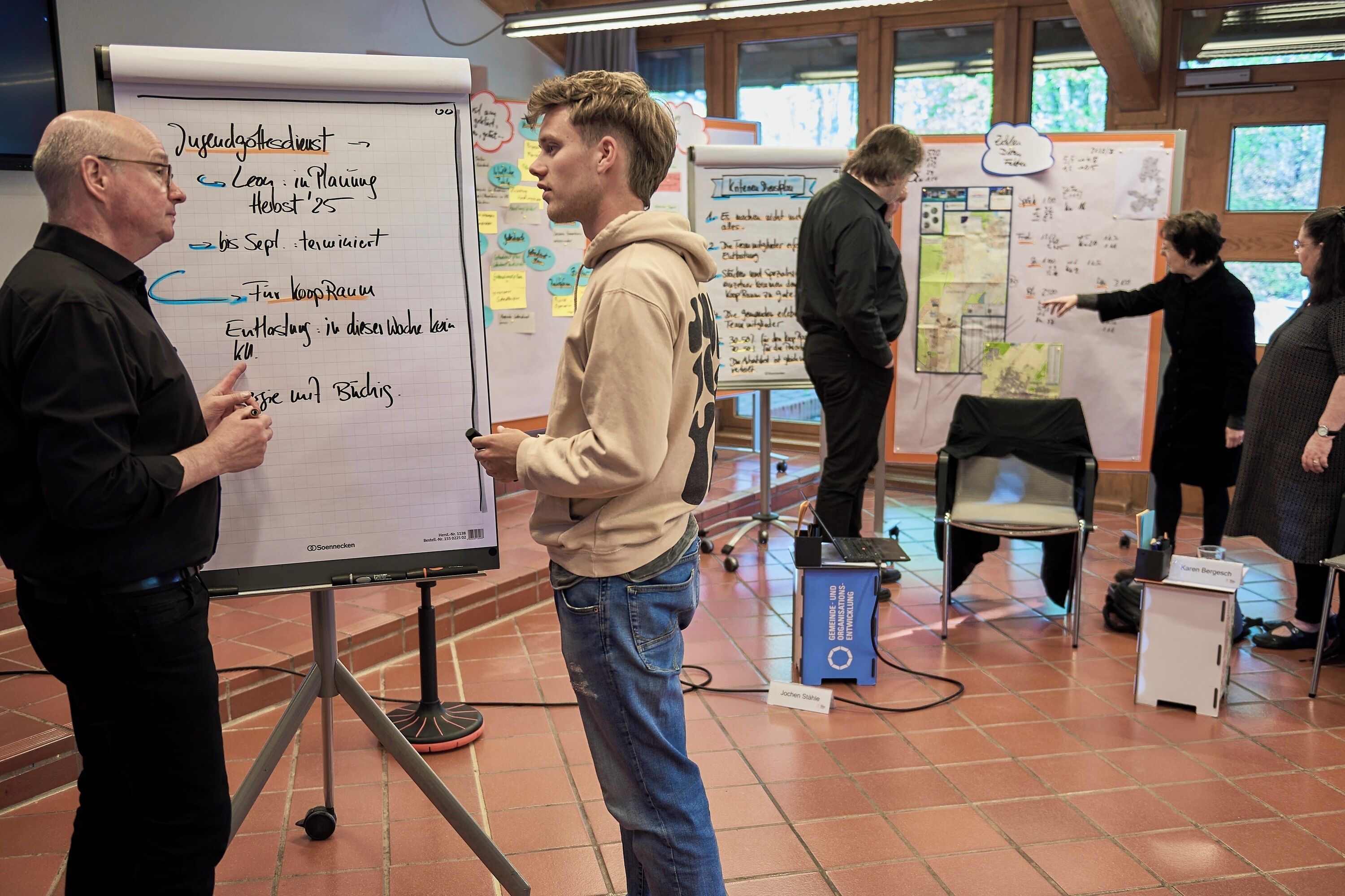 Eine Gruppe von Personen in einem Besprechungsraum mit Whiteboards, einem Laptop und einem Namensschild.