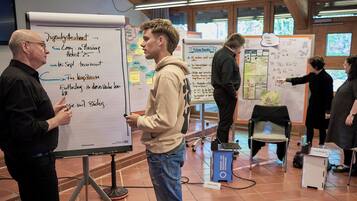 Eine Gruppe von Personen in einem Besprechungsraum mit Whiteboards, einem Laptop und einem Namensschild.