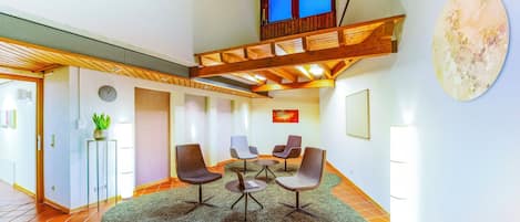 Una habitación amplia con techo alto, un balcón de madera, una mesa redonda con sillas y un cuadro abstracto de gran tamaño en la pared.
