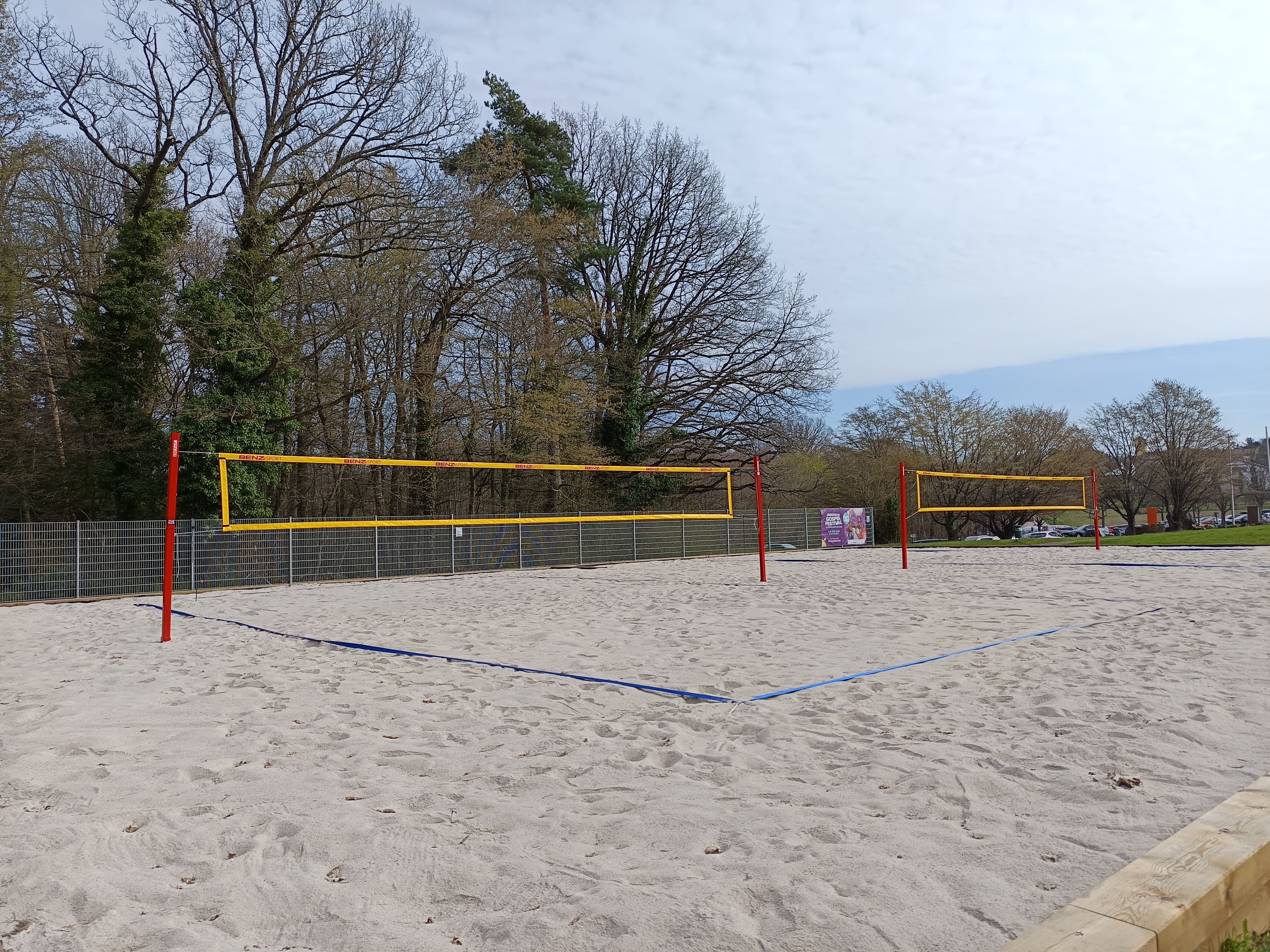 A volleyball court with a net, surrounded by a fence and trees.