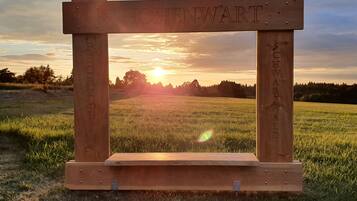 Un letrero de madera con los nombres 'HOHENWART' y 'SCHWARZWAD' grabados, sobre un fondo de atardecer.