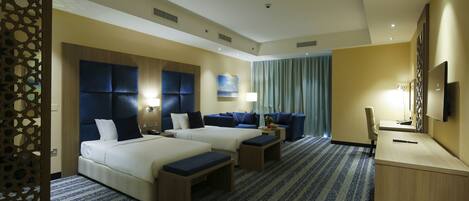 A hotel room with two beds, a desk, a chair, a TV, and a large window with curtains.