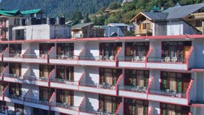 A multi-story hotel with balconies, a parking area, and a mountainous backdrop. - New Harmony Inn (Manali)