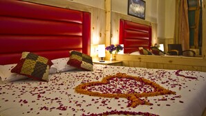 A hotel room with a red headboard, a heart-shaped flower arrangement on the bed, and a mirror reflecting the room's decor. - New Harmony Inn (Manali)