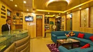 A hotel lobby with a reception desk, a blue sofa, and a television screen. - New Harmony Inn (Manali)
