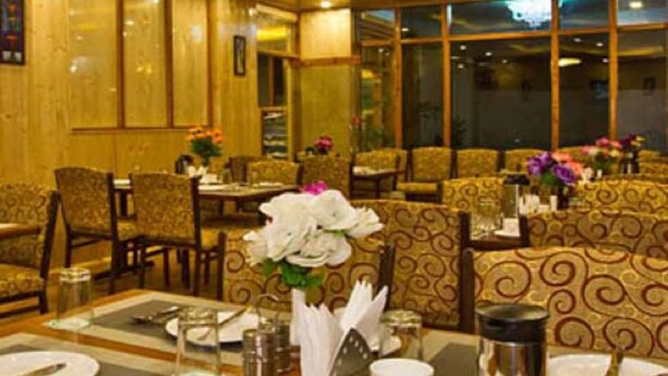 A dining area with tables set for two, featuring a wooden ceiling and patterned upholstery. - New Harmony Inn (Manali)