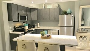 A modern kitchen with dark cabinets, stainless steel appliances, a marble countertop, and two upholstered chairs. - Spectacular  Ocean Front 1 Bedroom Villa in Golf community, Pal mas Del Mar  (Palmas Del Mar)