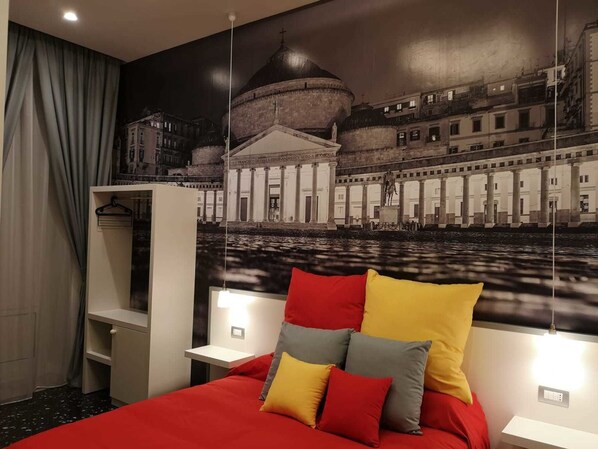 Una habitación de hotel con una cama grande, un armario, un escritorio y un mural de un edificio histórico.