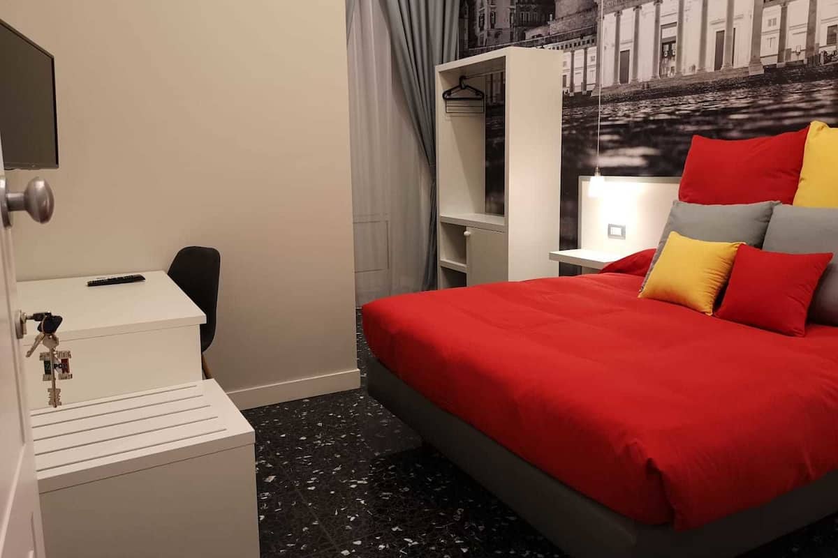 A hotel room with a bed, a desk, a chair, a wardrobe, and a wall-mounted TV.