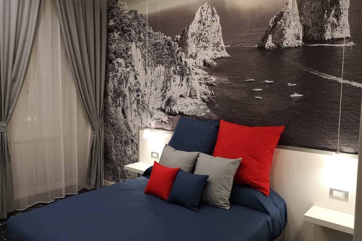 A bedroom with a bed, curtains, and a wall mural of a coastal scene.