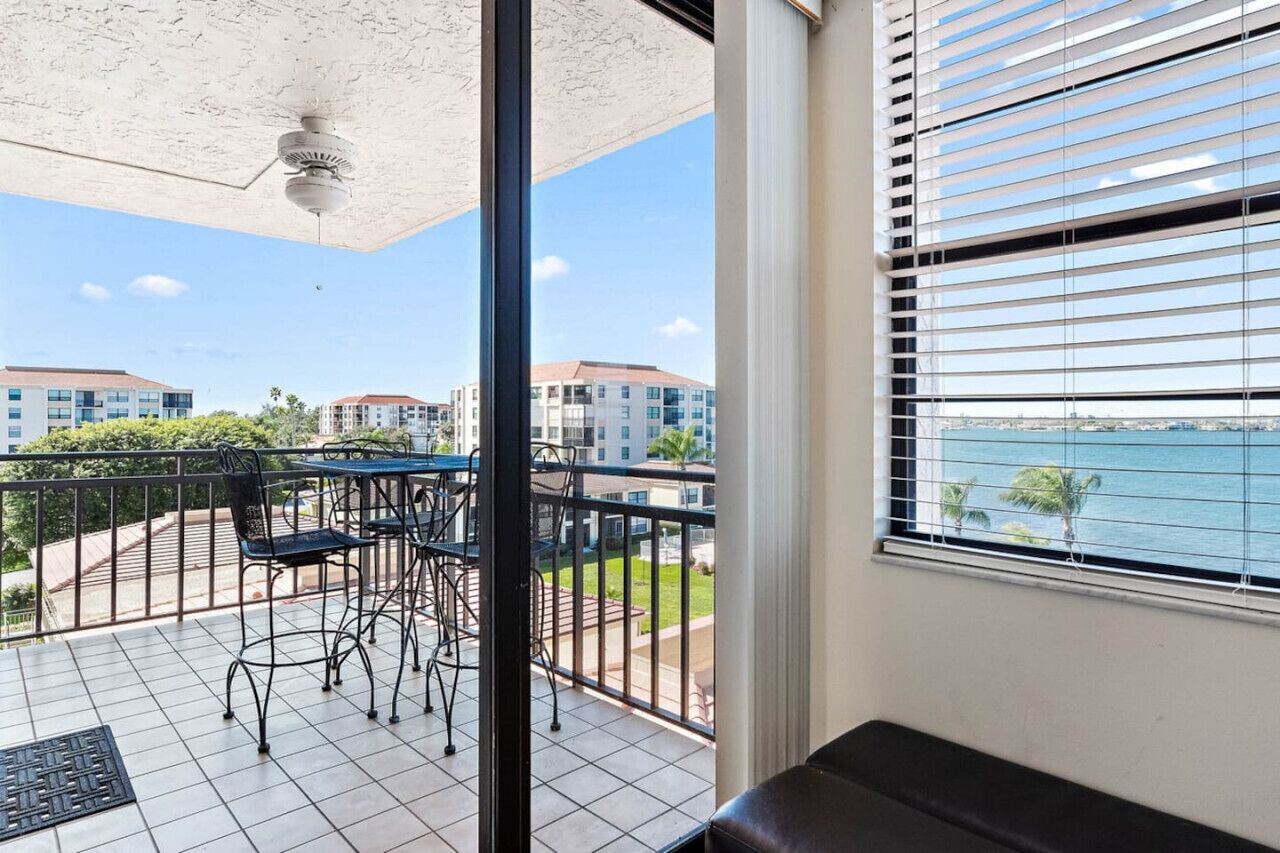 Un balcon avec une table et des chaises, un ventilateur de plafond et une vue sur les bâtiments et l’eau.