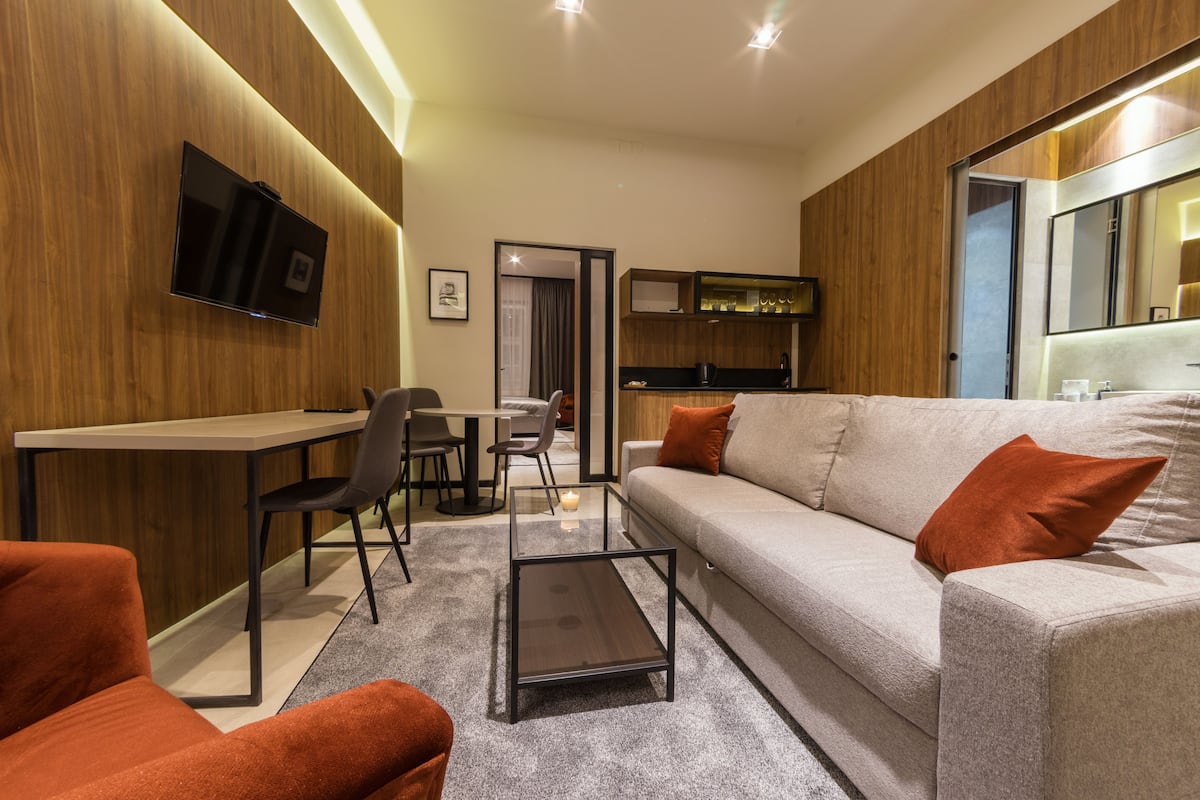 Ein modernes Wohnzimmer mit einer Couch, Sesseln, einem Couchtisch und einem an der Wand montierten Fernseher.