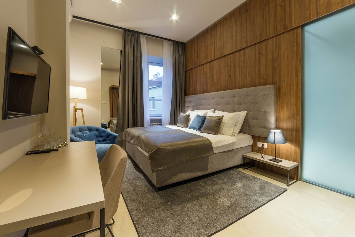 Ein modernes Hotelzimmer mit einem großen Bett, einem Schreibtisch, einem Sessel und einem Fernseher.