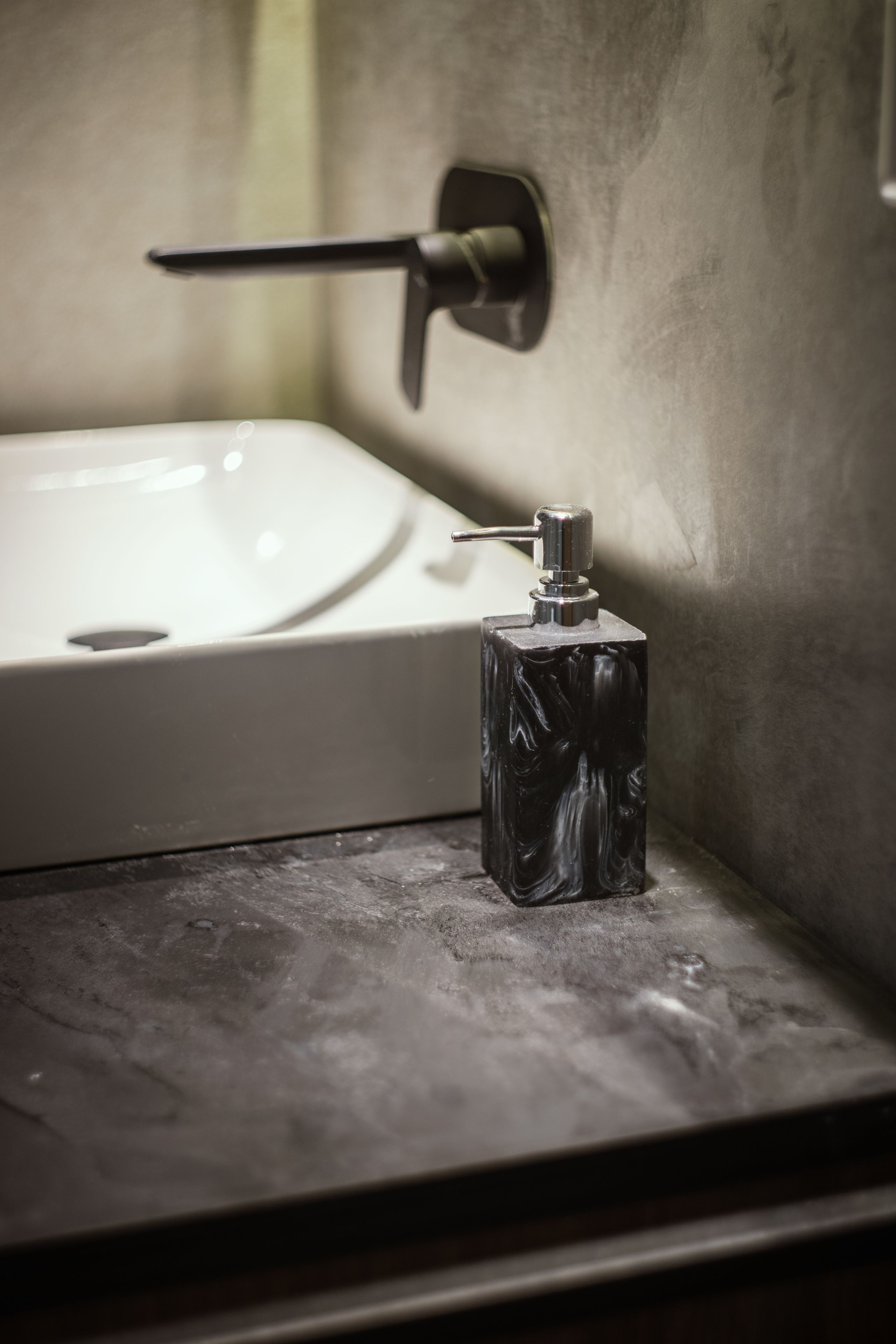 A bathroom with a white sink, a black marble soap dispenser, and a towel rack.