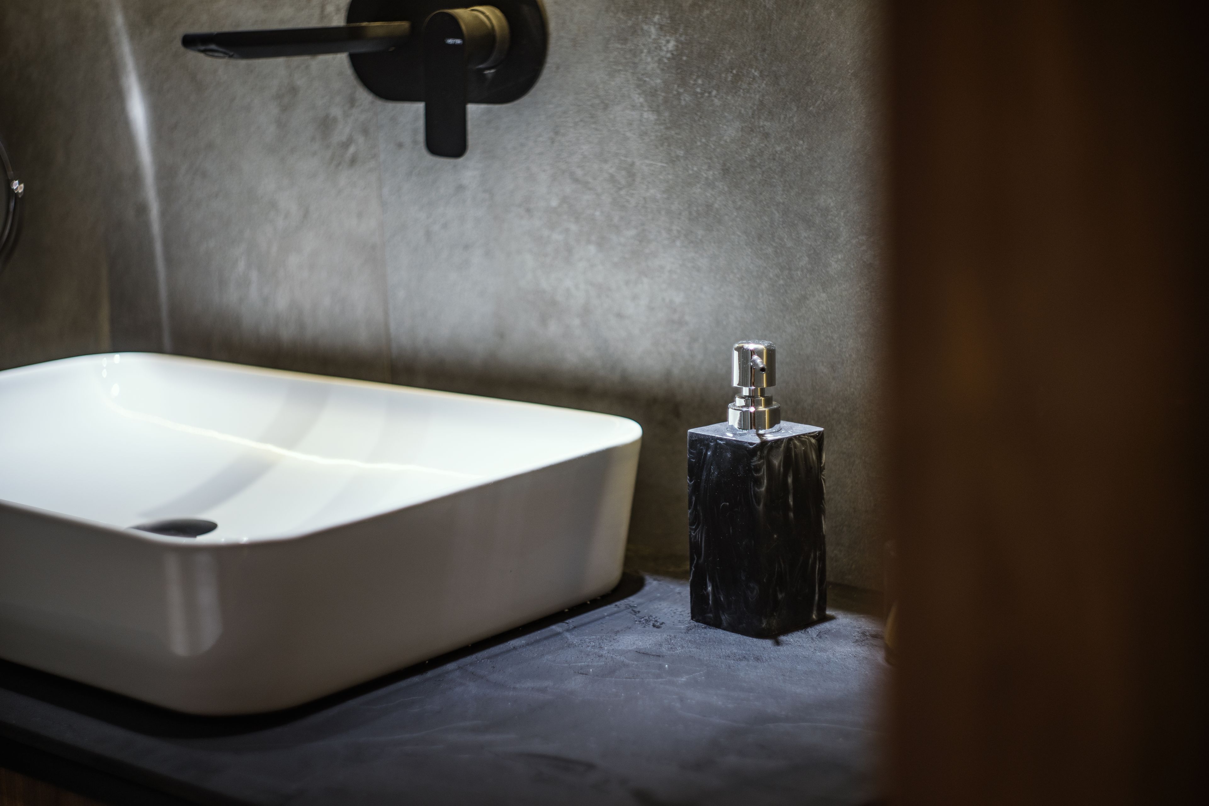 Un baño con un lavamanos blanco, un grifo negro y una pared con textura.