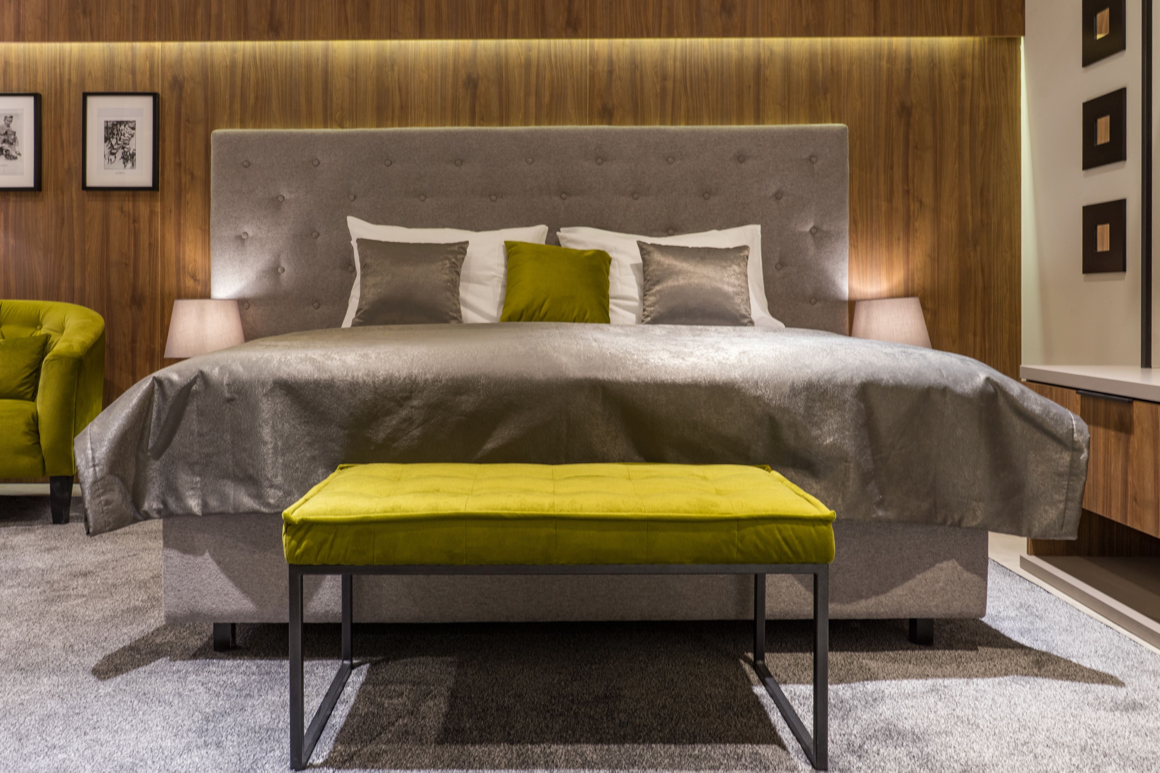 Quarto moderno com cama grande, um banquinho e uma parede de madeira com quadros.