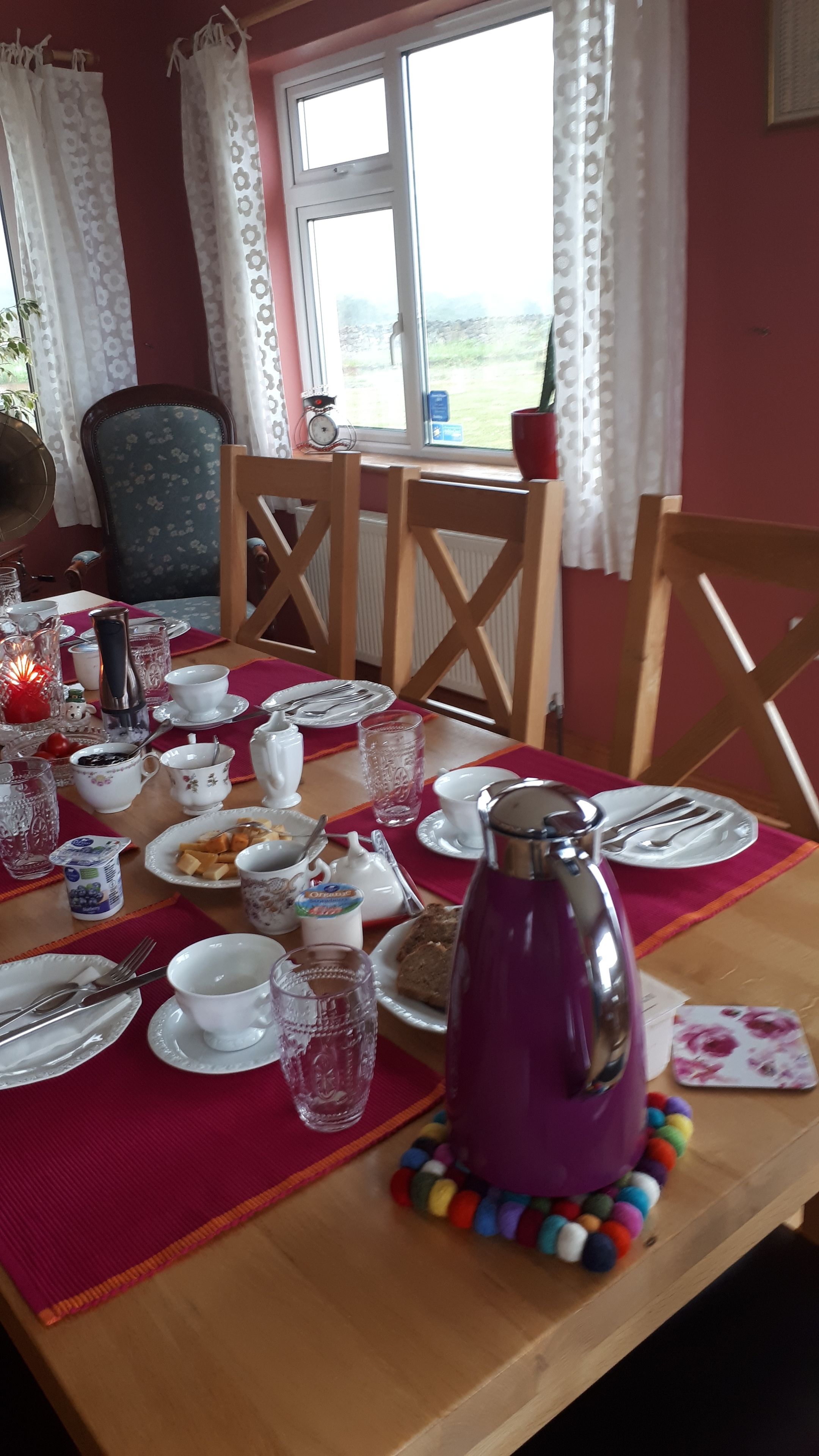A dining table set with plates, cups, and a kettle, with chairs around it.