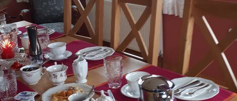 A dining table set with plates, cups, and a kettle, with chairs around it.