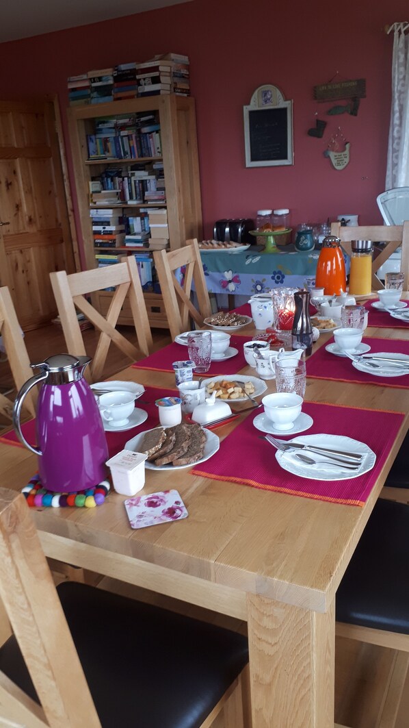 Una mesa de comedor preparada con platos, tazas y una cafetera, rodeada de sillas.