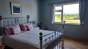 A bedroom with a bed, a nightstand, a window with curtains, and a view of greenery outside. - Tullaleagan Guesthouse (Oughterard)