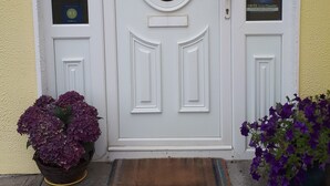 A white door with a glass panel, a doormat, and two potted plants. - Tullaleagan Guesthouse (Oughterard)