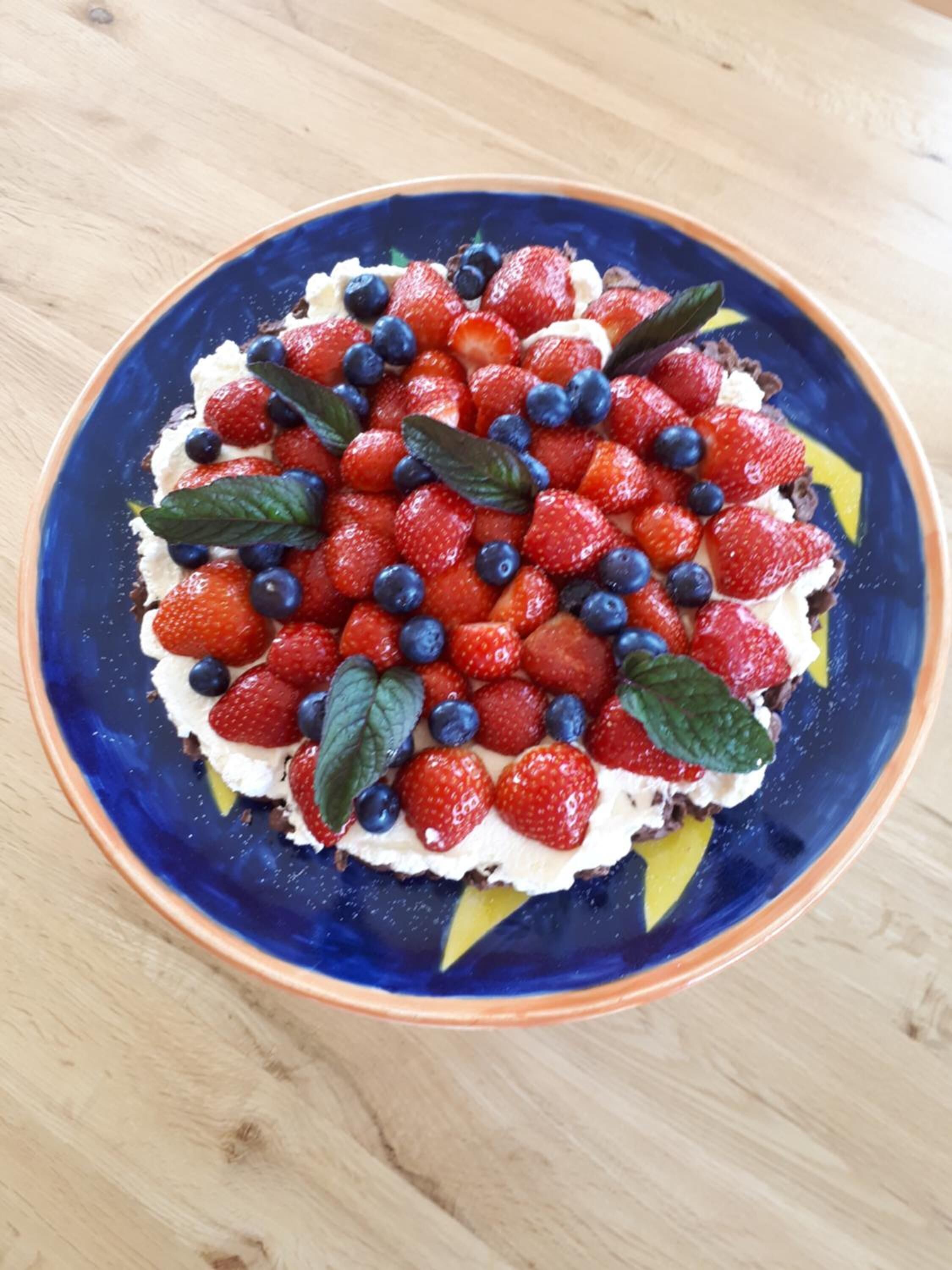 A dessert on a blue plate with strawberries and blueberries on top.