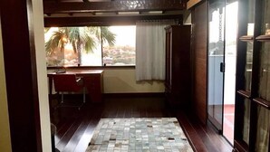A room with a tiled floor, a desk, a chair, a window with a view of palm trees, and a sliding glass door. - Casa Geribá (Búzios)