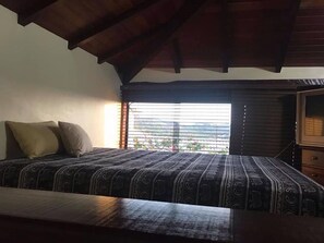 A bedroom with a bed, pillows, a window with blinds, and a wooden ceiling. - Casa Geribá (Búzios)