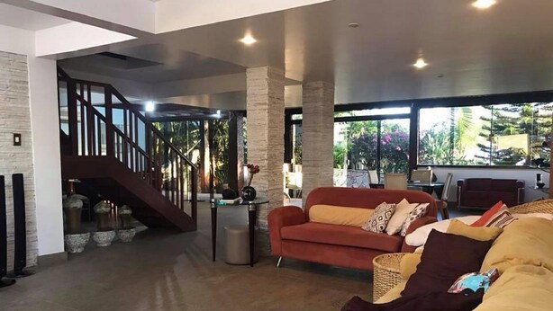 A spacious living area with a red sofa, a beige sofa, and a staircase leading to an upper level. - Casa Geribá (Búzios)