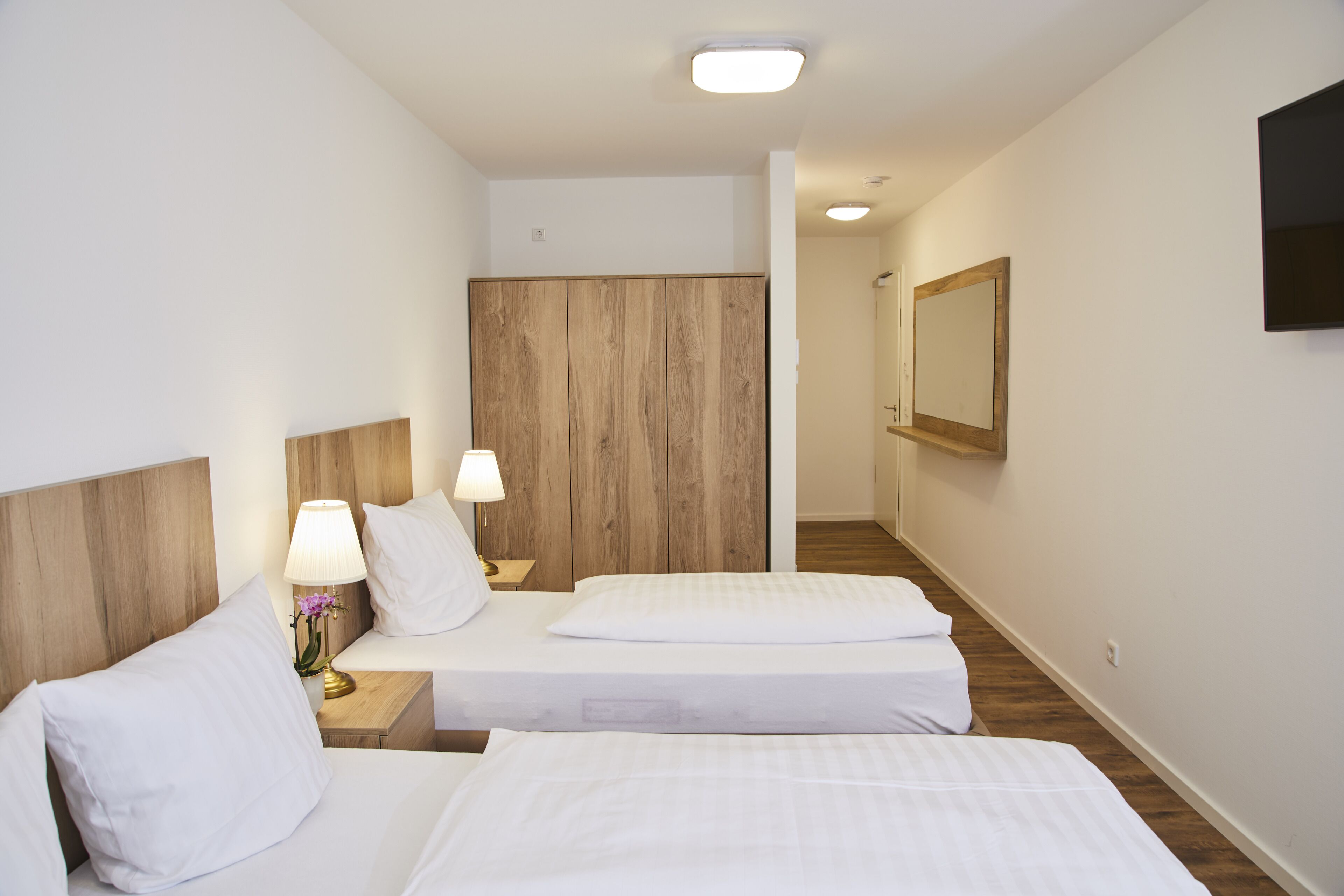 Una habitación de hotel con dos camas, un cabecero de madera, una mesita de noche con una lámpara y un espejo en la pared.