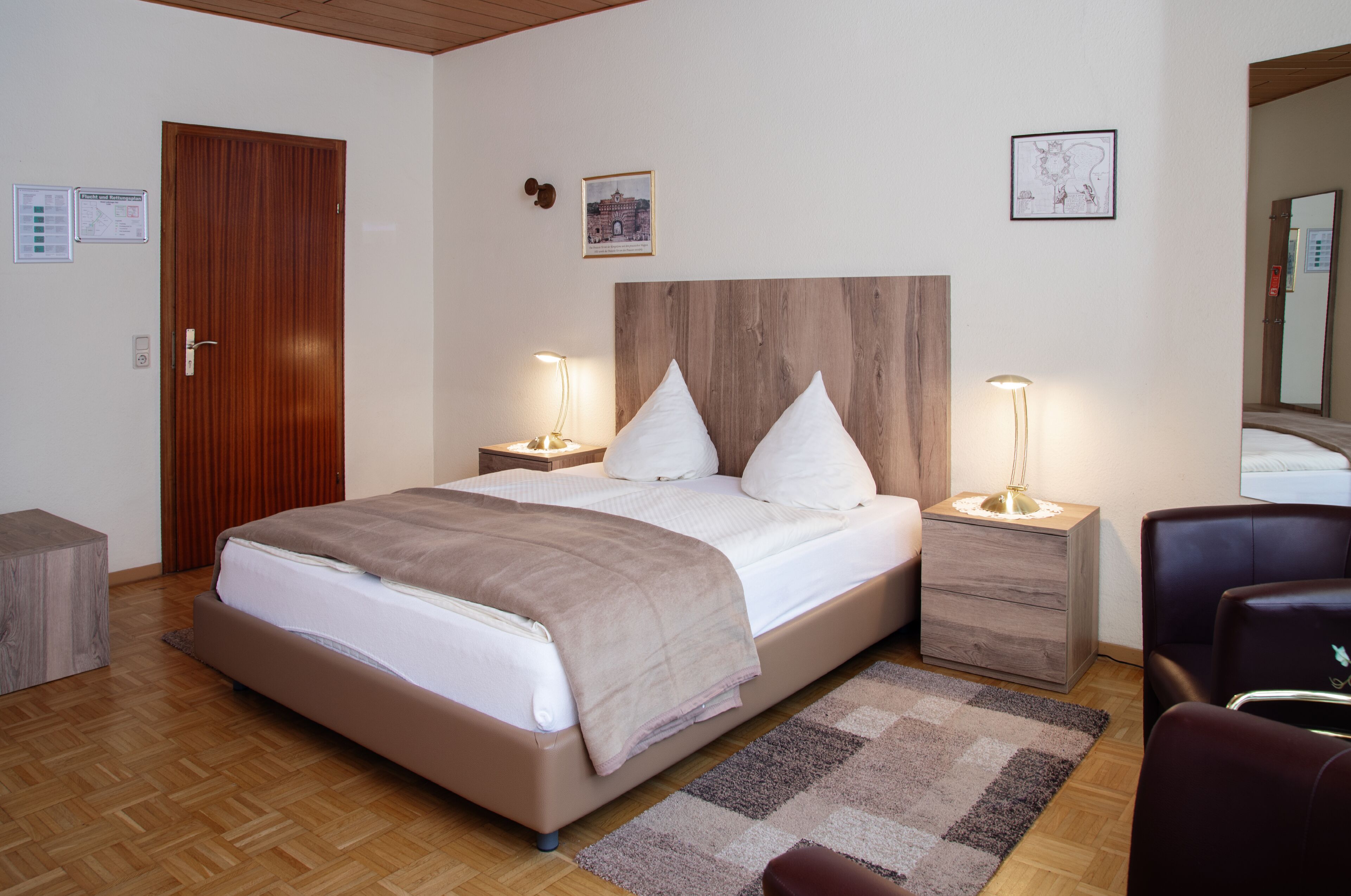 A neatly arranged bedroom with a wooden headboard, a large bed with white linens, two bedside tables with lamps, a wooden floor, and a small wooden stool.