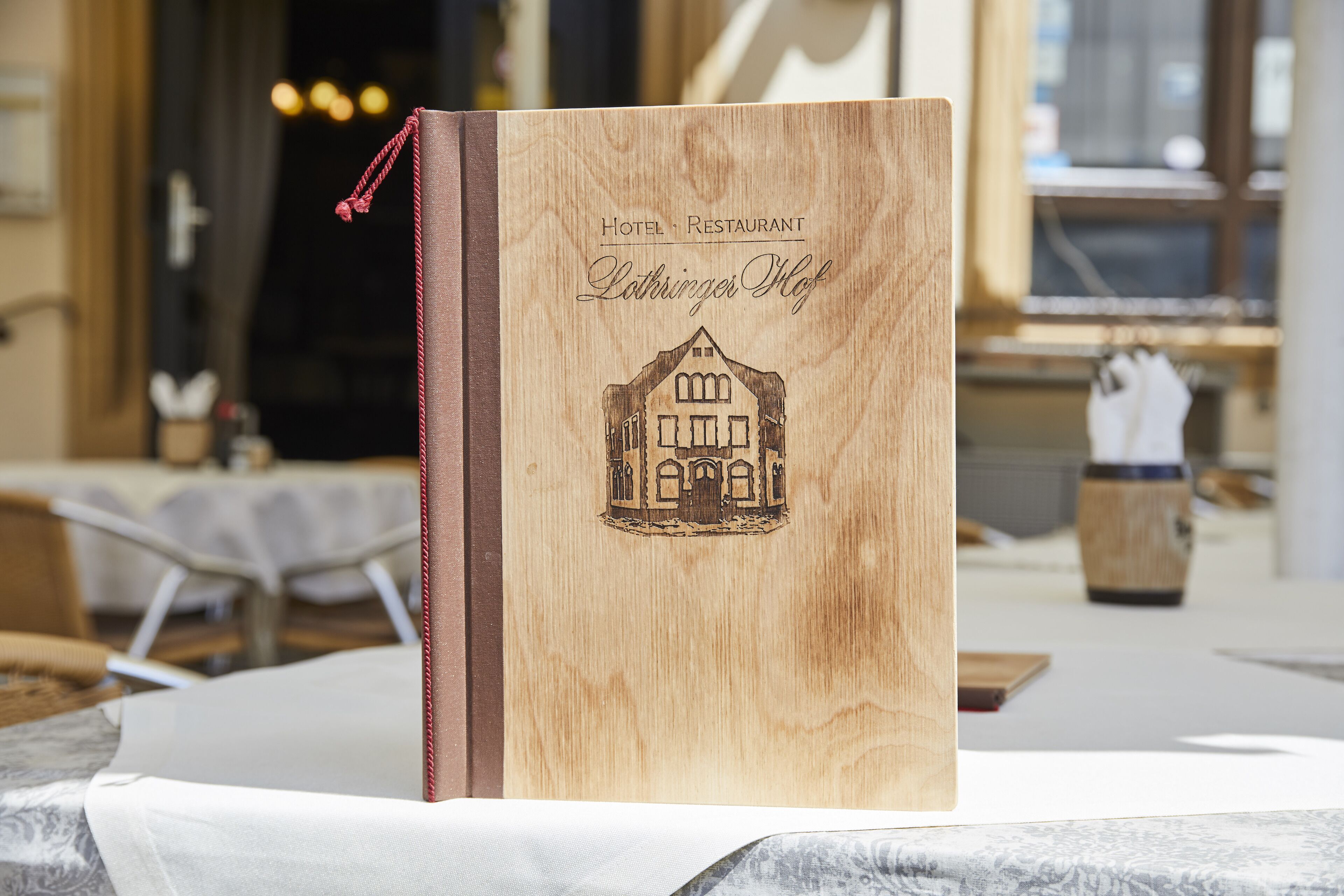 A wooden book with a house illustration and text reading "Hotel Restaurant Lothringer Hof".