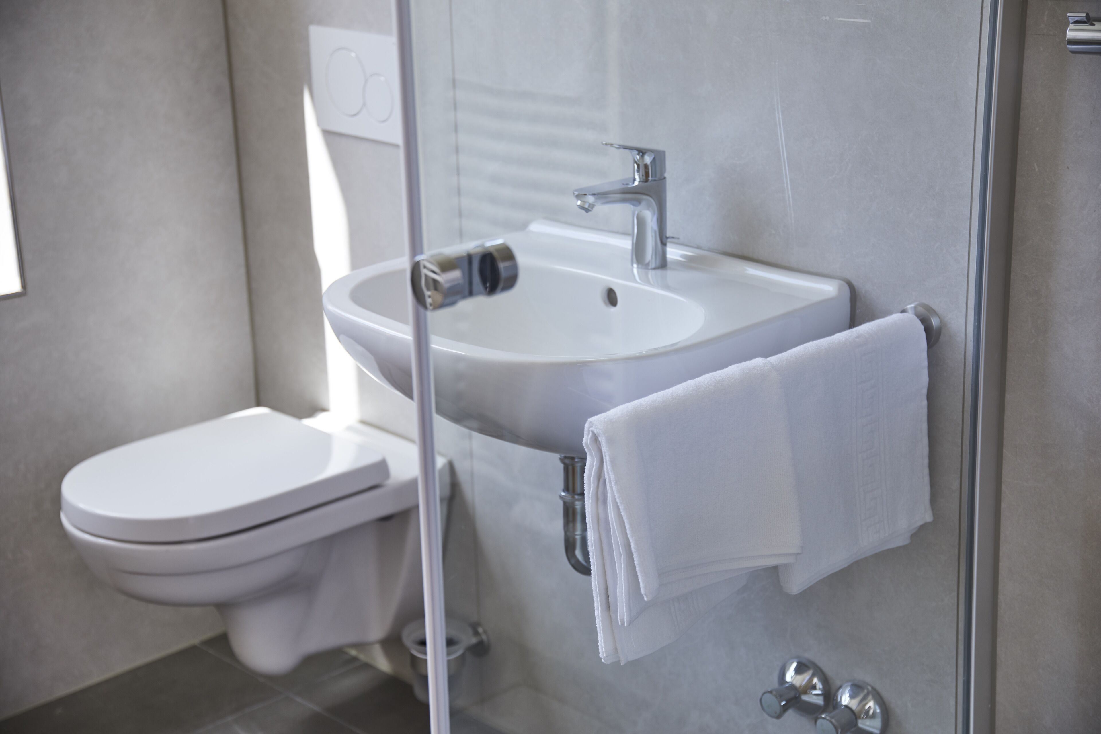 Un baño moderno con inodoro blanco, lavamanos con grifo y cabina de ducha de vidrio.