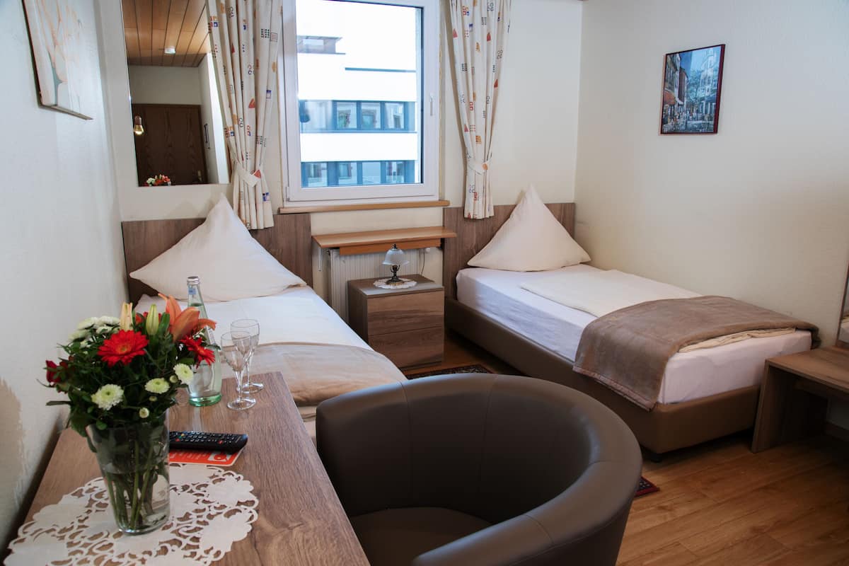 A hotel room with two beds, a desk with a vase of flowers, a chair, and a window with curtains.