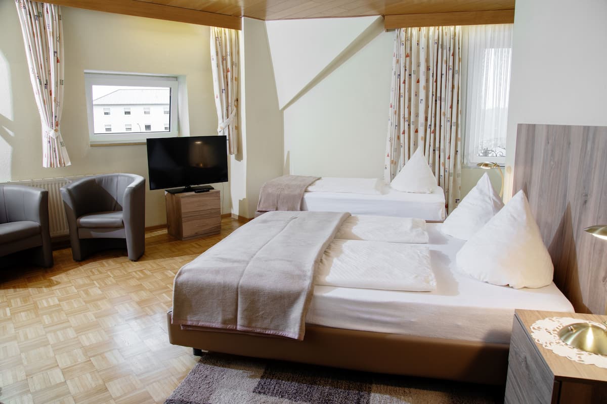 A hotel room with a bed, a TV, a chair, and a window.